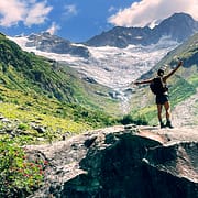 Über die Chakrenlehre Eine junge Frau steht auf einem Felsen in einem Alpen Hochtal und öffnet sich der schöpferischen Energie